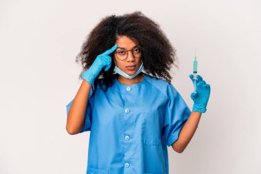 Genç Afro-Amerikan kıvırcık doktor elinde şırıngayla şakağı işaret ediyor, düşünüyor ve bir göreve odaklanıyor..