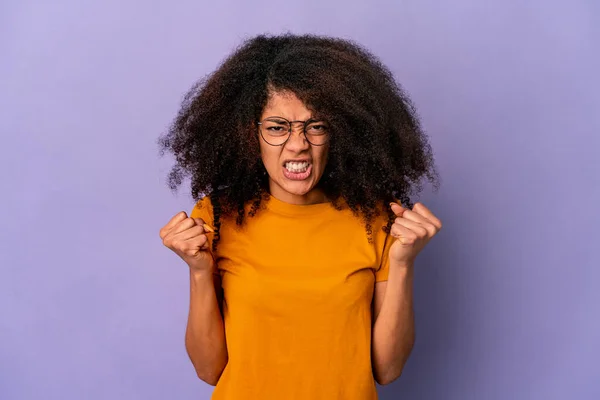 Young african american curly woman isolated on purple background showing fist to camera, aggressive facial expression.