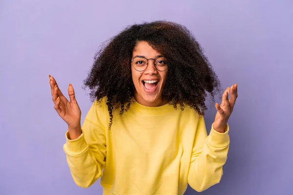 Young african american curly woman isolated on purple background receiving a pleasant surprise, excited and raising hands.