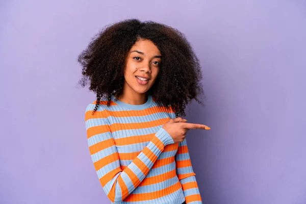 紫色の背景に孤立した若いアフリカ系アメリカ人の巻き毛の女性が笑顔で指摘し 何もない空間で何かを示す — ストック写真