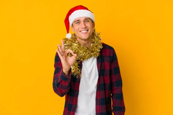 年轻的高加索人头戴圣诞礼帽 头戴黄色背景的礼物 开朗而自信地摆出一副不错的姿势 — 图库照片