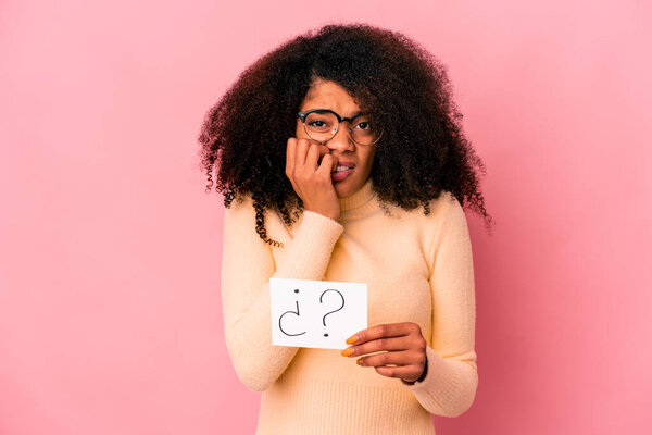 Young african american curly woman holding an interrogation on a placard biting fingernails, nervous and very anxious.