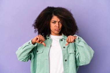 Genç Afro-Amerikalı kıvırcık kadın, mor arka planda izole edilmiş, hoş olmayan bir jest gösteriyor, başparmakları aşağıda. Anlaşmazlık konsepti.
