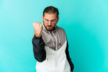 Uzun saçlı genç adam kameraya yumruğunu gösteriyor, agresif yüz ifadesi..