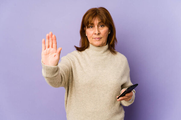 Кавказская женщина средних лет держит телефон с протянутой рукой, показывая стоп-сигнал, препятствуя вам.