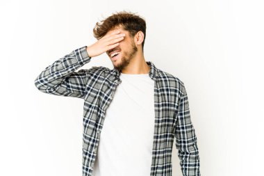 Beyaz arka plandaki genç Arap adam elleriyle gözlerini kapatıyor, gülümseyerek bir sürpriz bekliyor..