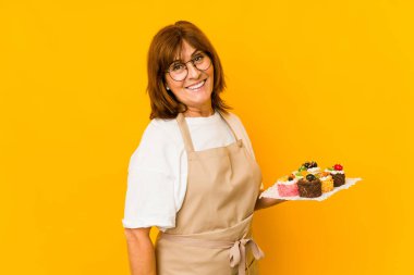 Orta yaşlı beyaz aşçı kadın gülümseyen, neşeli ve cana yakın bakışlarını yana çeviriyor..