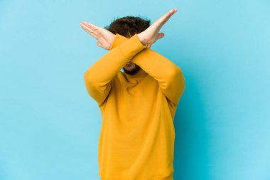 Mavi arka plandaki genç Arap adam iki kolu çapraz tutuyor, inkar kavramı.