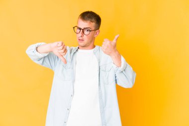 Kafkasyalı yakışıklı genç adam baş parmağını kaldırıyor ve baş parmak aşağı, zor seçim konsepti