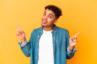 Genç Afro-Amerikalı kıvırcık adam, mor üzerine izole edilmiş, farklı fotokopi alanlarına bakıyor, birini seçiyor, parmaklarıyla gösteriyor..