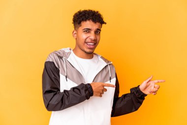 Genç Afro-Amerikan kıvırcık adamı, mor noktalar üzerinde izole edilmiş, bir fotokopi alanına işaret ediyor, heyecan ve arzusunu ifade ediyor..