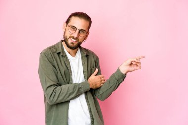 Uzun saçlı genç adam işaret parmağıyla işaret ederek gülümsüyor..