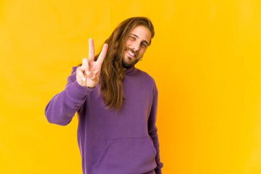 Uzun saçlı genç adam zafer işareti gösteriyor ve gülümsüyor..