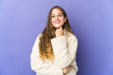 Genç beyaz, tatlı bir kadın gülümsüyor mutlu ve kendinden emin, çenesine elle dokunuyor..