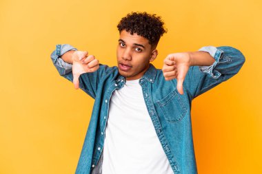 Genç Afro-Amerikalı kıvırcık adam, mor üzerine izole edilmiş, baş parmağını aşağı gösteren ve hoşlanmadığını ifade eden..