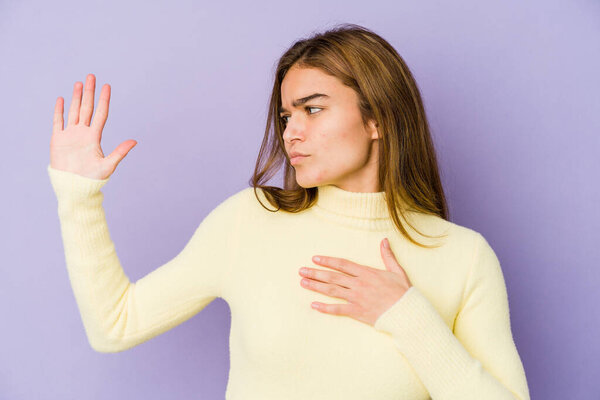Young skinny caucasian girl teenager on purple background taking an oath, putting hand on chest.