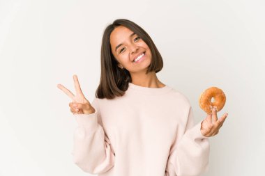 Genç İspanyol kadın çörek yiyor neşeli ve kaygısız parmaklarıyla barış sembolü gösteriyor..