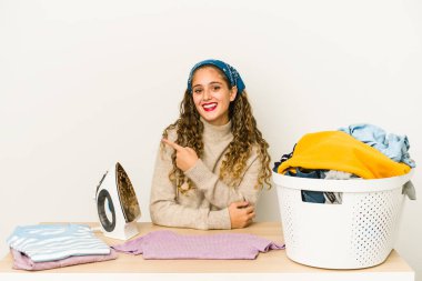 Giysileri ütüleyen beyaz bir kadın izole edilmiş, gülümseyen ve işaret eden, boş alanda bir şeyler gösteren..