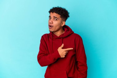 Genç Afro-Amerikalı kıvırcık adam mavi üzerine izole edilmiş gülümsüyor ve boş uzayda bir şeyler gösteriyor..