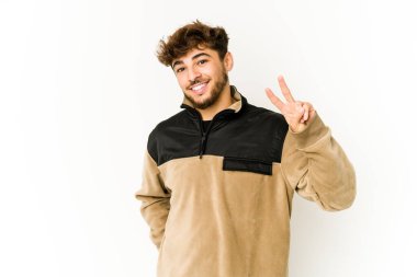 Beyaz arka planda genç bir Arap zafer işareti gösteriyor ve gülümsüyor..