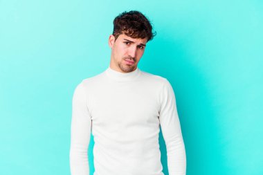 Kafkasyalı genç adam mavi arka planda izole edilmiş üzgün, ciddi yüzlü, mutsuz ve hoşnutsuz..