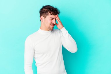 Kafkasyalı genç bir adam mavi arka planda izole edilmiş, başı ağrıyor, yüzüne dokunuyor..