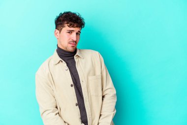 Mavi arka planda soyutlanmış genç beyaz bir adam gülümsüyor, neşeli ve keyifli görünüyor..