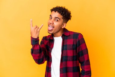 Genç Afro-Amerikalı kıvırcık adam, mor üzerine izole edilmiş, parmaklarıyla kaya hareketi yapıyor.