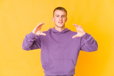 Beyaz tenli yakışıklı bir adam elinde avuç içi bir şeyle kameraya sunuyor..