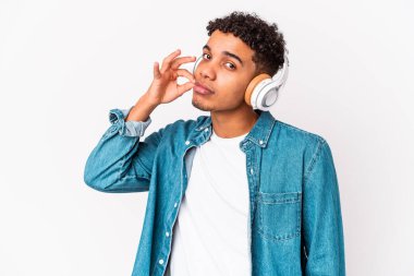 Genç Afro-Amerikalı kıvırcık adam izole edilmiş müzik dinliyor kulaklıklarıyla dudakları parmaklarıyla bir sır saklıyor.