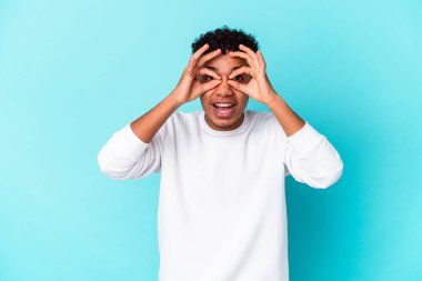 Genç Afro-Amerikalı kıvırcık adam mavi üzerine izole edilmiş gözlerinde sorun yok işareti var.