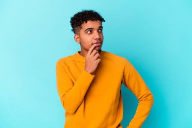Genç Afro-Amerikan kıvırcık adamı şüpheli ve şüpheci bir ifadeyle mavi bir tarafa bakıyor..