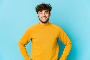 Mavi arka plandaki genç Arap adam ellerini kalçasından ayırmıyor..