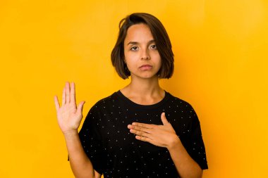 Genç İspanyol kadın sarıda izole edilmiş yemin ediyor, elini göğsüne koyuyor..