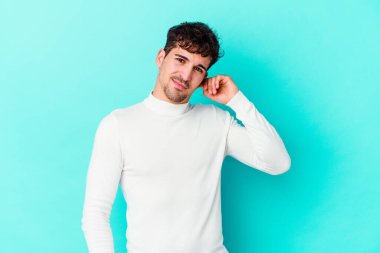 Genç beyaz adam mavi arka planda izole edilmiş parmaklarıyla kulaklarını kapatıyor, gürültülü bir ortam tarafından stresli ve umutsuz..