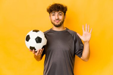 Genç futbolcu Hintli adam gülümseyerek beş numarayı parmaklarıyla gösteriyor..