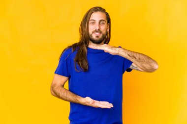 Uzun saçlı genç adam iki eliyle bir şey tutuyor, ürün sunumu..