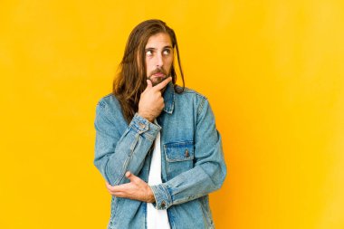 Uzun saçlı genç adam şüpheli ve kuşkulu bir ifadeyle yana bakıyor..