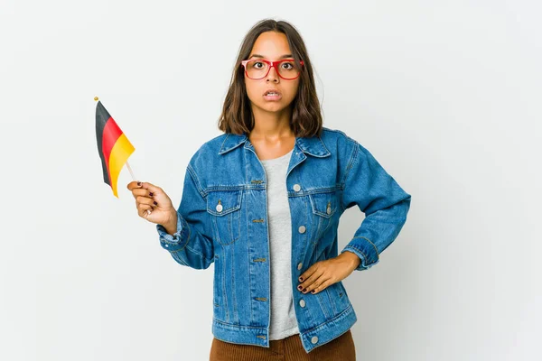白い背景にドイツ国旗を掲げた若いラテン系の女性がショックを受けている — ストック写真