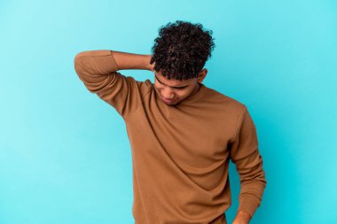 Genç Afro-Amerikalı kıvırcık adam, mavi üzerine izole edilmiş. Stres yüzünden boynu ağrıyor, masaj yapıyor ve elle dokunuyor..