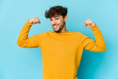 Mavi arka plandaki genç Arap adam güçlü bir hareket gösteriyor. Kollarıyla, kadınsı gücün sembolü.