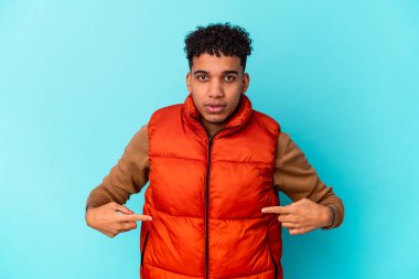 Genç Afro-Amerikan kıvırcık adamı, mavi kişinin üzerinde izole edilmiş bir şekilde gömlek fotokopi alanını gösteriyor, gururlu ve kendinden emin.