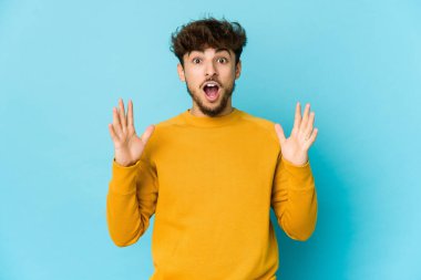 Mavi arka plandaki genç Arap bir zaferi ya da başarıyı kutluyor. Şaşırdı ve şok oldu..