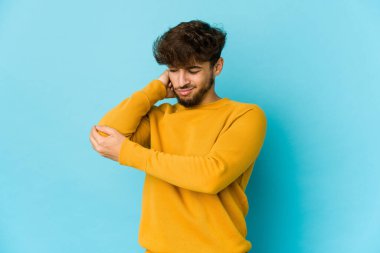 Mavi arka planda genç bir Arap, dirsek masajı yapıyor, kötü bir hareketin ardından acı çekiyor..