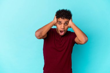 Genç Afro-Amerikalı kıvırcık adam, mavi kulaklarla izole edilmiş, elleri kulaklarda, çok fazla ses duymamaya çalışıyor..