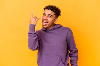 Genç Afro-Amerikalı kıvırcık adam, mor üzerine izole edilmiş, parmaklarıyla kaya hareketi yapıyor.