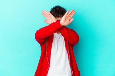 Kafkasyalı genç adam mavi arka planda izole edilmiş iki kolu çapraz tutuyor, inkar kavramı.