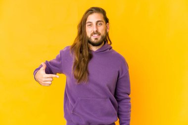 Uzun saçlı genç bir adam gömleğin fotokopi odasını elle işaret ediyor, gururlu ve kendinden emin.