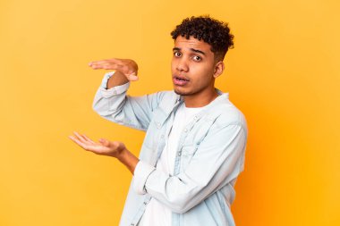 Genç Afro-Amerikalı kıvırcık adam mor üzerine izole edilmiş iki eliyle bir şey tutuyor, ürün sunumu..