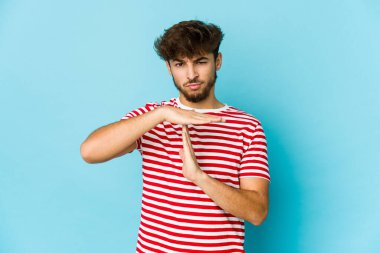 Mavi arka plandaki genç Arap adam bir mola hareketi gösteriyor.